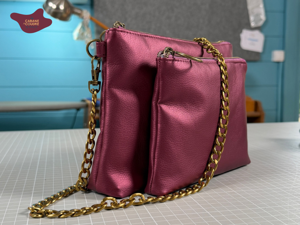 Pour le **texte alternatif**, je resterais descriptif tout en intégrant naturellement le nom et ton mot-clé SEO :
Sac 3-en-1 Léna cousu en simili cuir rose métallisé, composé de deux trousses et porté avec une bandoulière chaîne dorée.